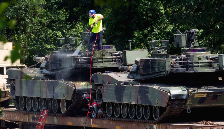 FILE - A worker uses pressure washer to clean an Abrams tanks on a flat car in a rail yard in D.C.