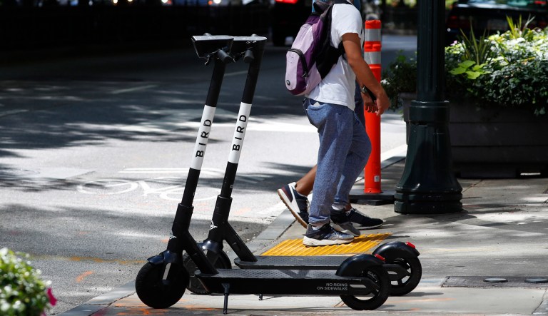 Pedestrians walk past electric scooters.