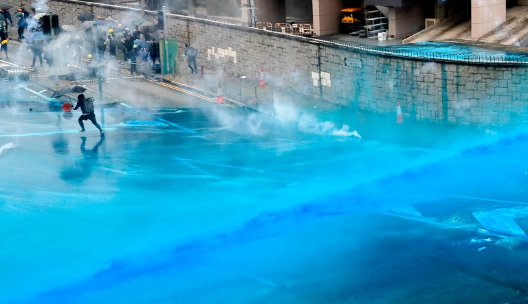Police fire blue-colored water from water cannons at protesters in Hong Kong on Saturday. While other protesters marched back and forth elsewhere in the city, a large crowd wearing helmets and gas masks gathered outside the city government building. 