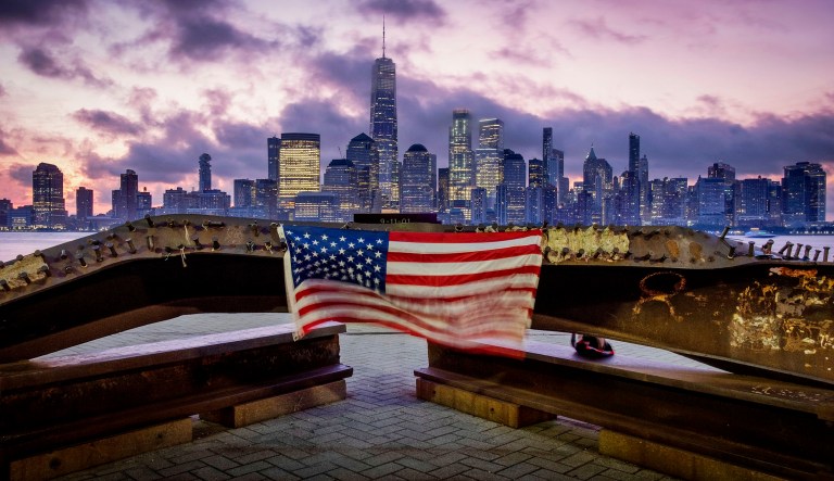 A U.S. Flag hanging from a steal girder, damaged in the Sept. 11, 2001 attacks on the World Trade Center, blows in the breeze at a memorial in Jersey City, N.J., Sept. 11, 2019 as the sun rises behind One World Trade Center building and the re-developed area where the Twin Towers of World Trade Center once stood in New York City on the 18th anniversary of the attacks.