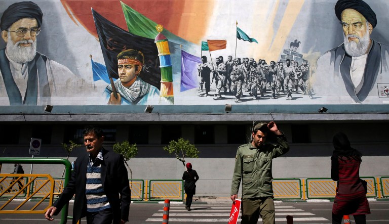 Pedestrians cross the Enqelab-e-Eslami (Islamic Revolution) street under a mural depicting the late Iranian revolutionary founder Ayatollah Khomeini, right, members of Basij paramilitary force, center, and Supreme Leader Ayatollah Ali Khamenei, in Tehran, Iran, Tuesday, March 31, 2015. 