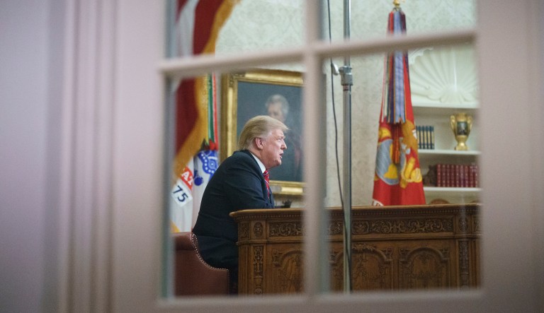 President Trump is seen though the window of the Oval Office of the White House in Washington, Tuesday, Jan. 8, 2019, as he addresses the nation.