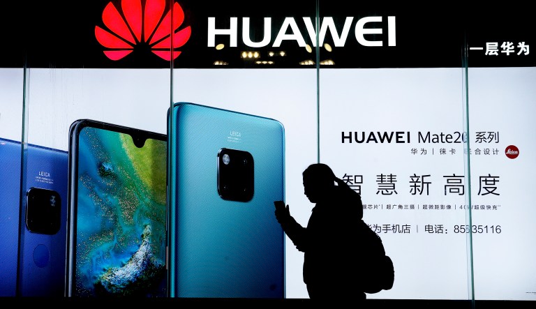 In this Dec. 11, 2018, file photo, a woman browses her smartphone as she walks by a Huawei store at a shopping mall in Beijing. 
