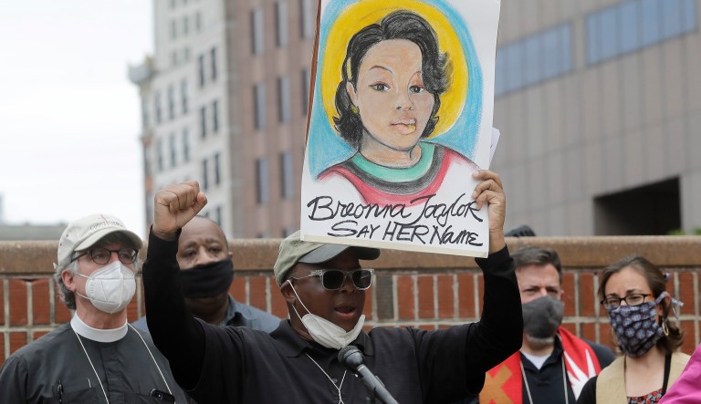 Kevin Peterson, the founder and executive director of the New Democracy Coalition, center, displays a placard showing Breonna Taylor as he addresses a rally.