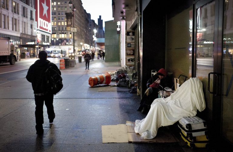 FILE - A homeless person sleeps under a blanket while seated on a New York sidewalk.  New York City officials are planning to remove makeshift shelters set up by homeless people on city streets, mirroring similar efforts in other liberal metropolises that had previously tolerated the encampments. Mayor Eric Adams disclosed the initiative in an interview with The New York Times on Friday, March 25, 2022, but provided few details. (AP Photo/Mark Lennihan, File)