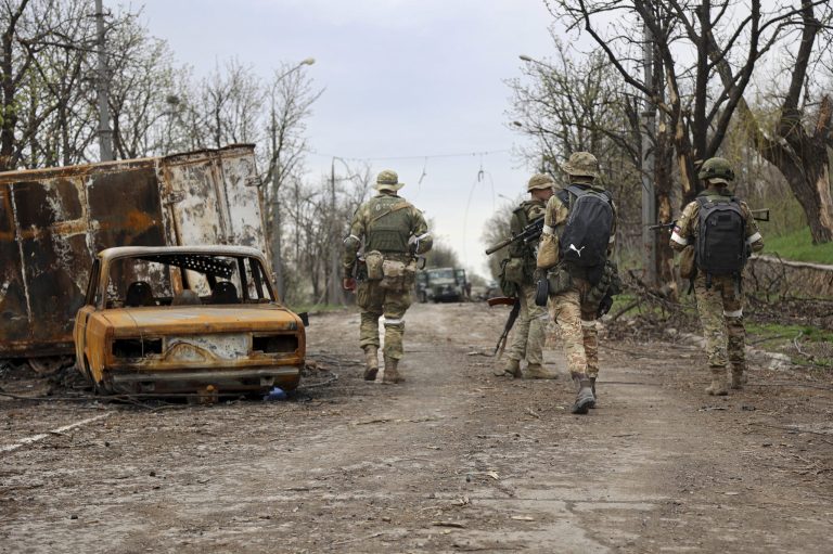 Servicemen of Donetsk People's Republic militia walk past damaged vehicles during a heavy fighting in an area controlled by Russian-backed separatist forces in Mariupol, Ukraine, Tuesday, April 19, 2022. 
