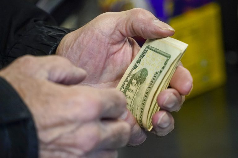 A customer thumbs through his money as he buys tickets for the Monday Powerball drawing for an annuity value of at least $1.9 billion, Monday, Nov. 7, 2022, at a convenience store in Renfrew, Pennsylvania. (AP Photo/Keith Srakocic)