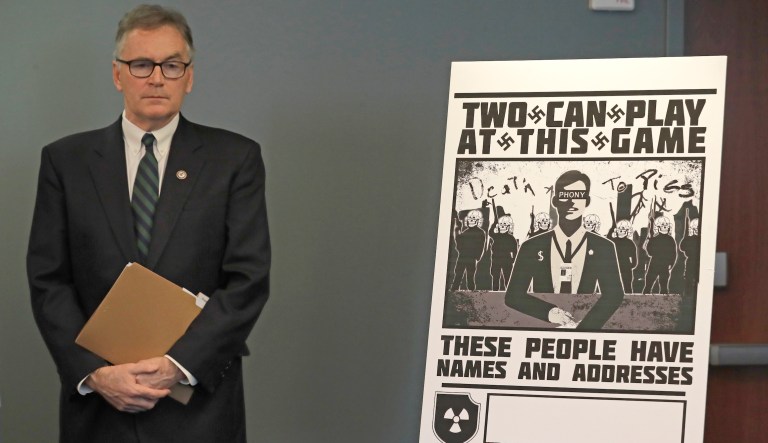 U.S. Attorney Brian Moran stands next to a poster that was mailed earlier in the year to the home of Chris Ingalls, an investigative reporter with KING-TV in Seattle, Wednesday, Feb. 26, 2020, during a news conference in Seattle. Moran and other officials announced charges Wednesday against a group of alleged members of the neo-Nazi group Atomwaffen Division for cyber-stalking and mailing threatening communications â including Swastika-laden posters â in a campaign against journalists in several cities.