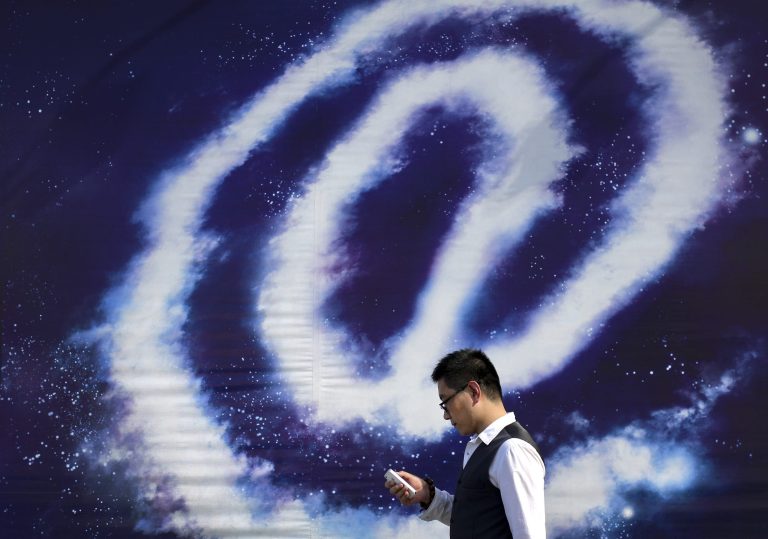 A Chinese man checking on his smartphone walks past an 