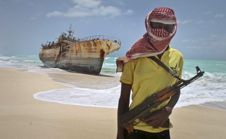   FILE - In this Sunday, Sept. 23, 2012 file photo, masked Somali pirate Hassan stands near a Taiwanese fishing vessel that washed up on shore after the pirates were paid a ransom and released the crew, in the once-bustling pirate den of Hobyo, Somalia. A U.K.-led Piracy Ransom Task Force says the shipping industry must adopt additional measures to ensure that payments aren't made to pirates after a successful attack. (AP Photo/Farah Abdi Warsameh, File)  