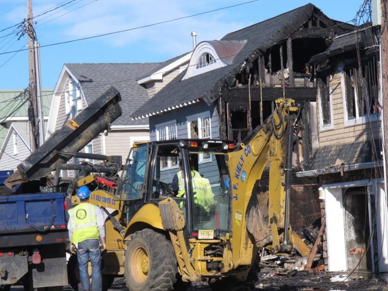   Work crews use heavy machinery to remove debris from homes damaged by Superstorm Sandy, across the street from the scene of a fire that damaged 12 homes on Wednesday, Dec. 5, 2012. The front-end loader was picking up debris from a house across the street from the blaze that was damaged by flooding from the storm but not by the fire in this traumatized Jersey shore town. The flood cleanup continued even as investigators tried to determine what sparked the blaze. (AP Photo/Wayne Parry)  