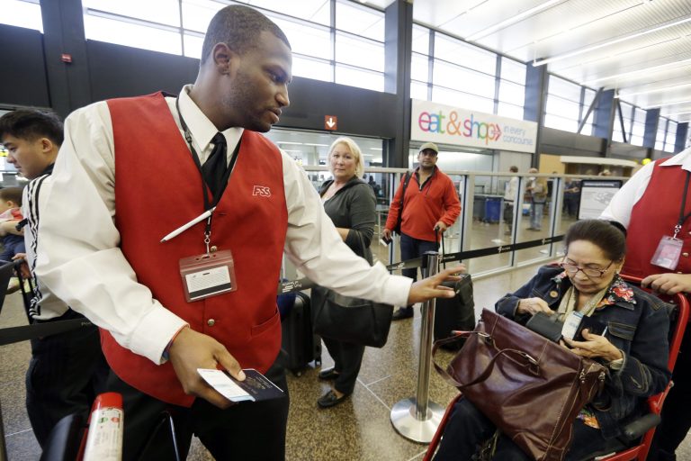 In this Tuesday, Oct. 22, 2013 photo, wheelchair attendant Erick Conley, left, assists an elderly passenger heading overseas at Seattle-Tacoma International Airport in SeaTac, Wash. A Washington state judge has struck part of the voter-approved $15 an hour minimum wage measure for airport workers in SeaTac. (AP Photo/Elaine Thompson)