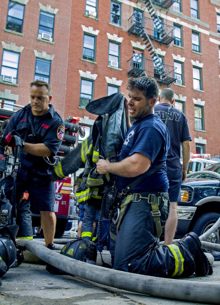 An FDNY firefighter kneels as he removes his turnout gear after exiting a building while fighting a multi alarm fire on West 136th Street in the Hamilton Heights neighborhood of New York, Monday, Aug. 18, 2014. Officials say the fire was on the second and third floors of the six-story building. (AP Photo/Craig Ruttle)
