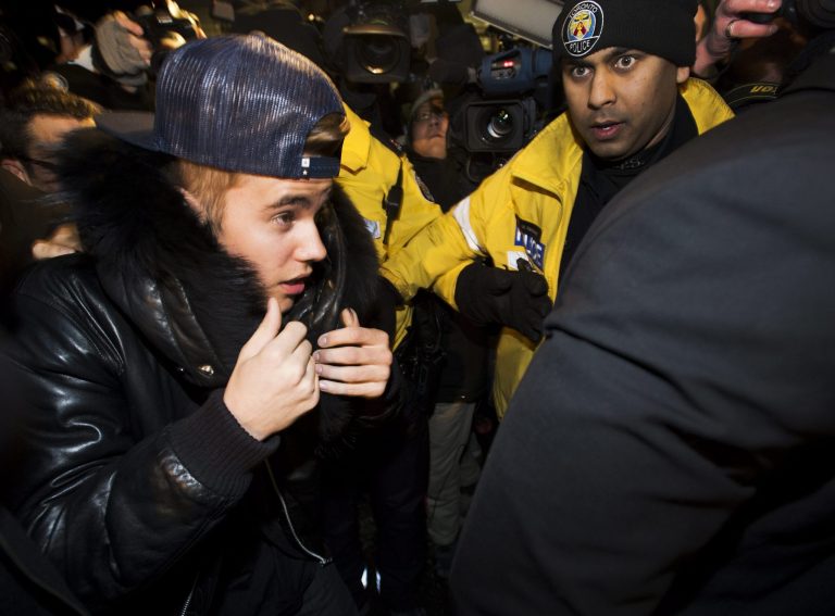 Canadian musician Justin Bieber is swarmed by media and police officers as he turns himself into city police for an expected assault charge, in Toronto, on Wednesday, Jan. 29, 2014. A police official said the charge has to do with an alleged assault on a limo driver in December. (AP Photo/The Canadian Press, Nathan Denette)