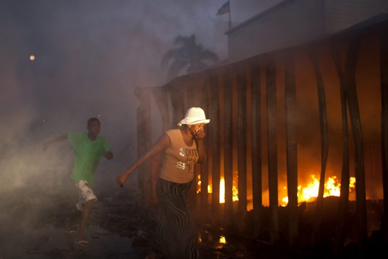   A woman covers her mouth and nose as she walks past an active fire at Port Market in Port-au-Prince, Haiti, Saturday Dec. 29, 2012. Police spokesman Frantz Lerebours said Saturday that dozens of stalls at the popular marketplace were burned to the ground and that few items were recovered. Authorities are investigating what caused the fire late Friday. (AP Photo/Dieu Nalio Chery)  