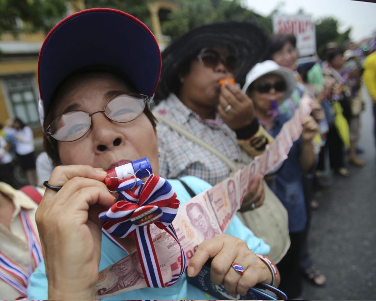 An anti-government protester blows a whistle and show money which they will donate to their leader Suthep Thaugsuban during a march through streets in Bangkok, Thailand, Monday, May 19, 2014.  Thailand's political crisis deepened last week when the Constitutional Court removed Prime Minister Yingluck Shinawatra for nepotism along with nine Cabinet members in a case that many viewed as politically motivated. Protesters say Yingluck's removal is not enough, though. She was simply replaced by Niwattumrong, who was a deputy premier from the ruling party.(AP Photo/Sakchai Lalit)