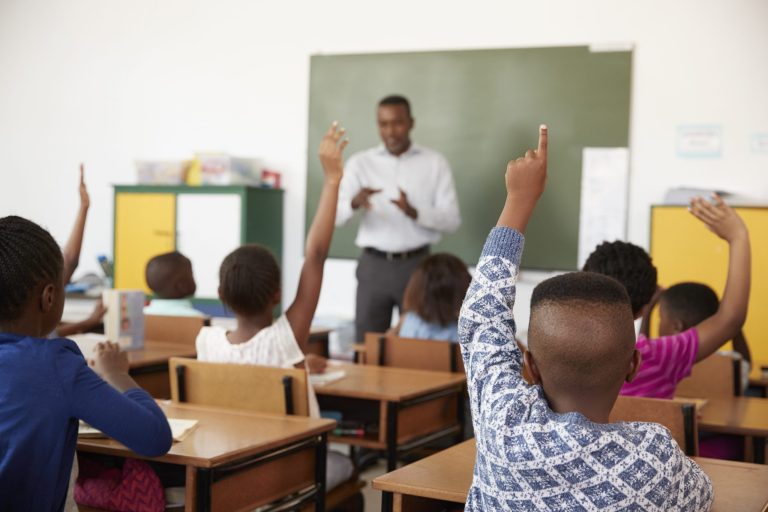 education, elementary school, learning and people concept - group of school kids with teacher sitting in classroom and raising hands