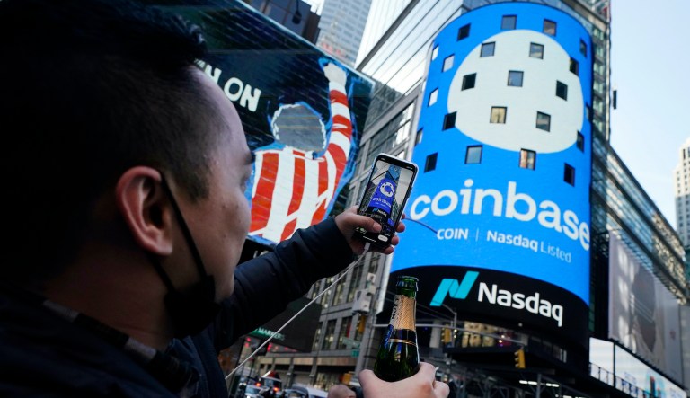 Coinbase employee Daniel Huynh holds a celebratory bottle of champagne as he photographs outside the Nasdaq MarketSite, in New York's Times Square, Wednesday, April 14, 2021. Wall Street will be focused on Coinbase Wednesday with the digital currency exchange becoming a publicly traded company.