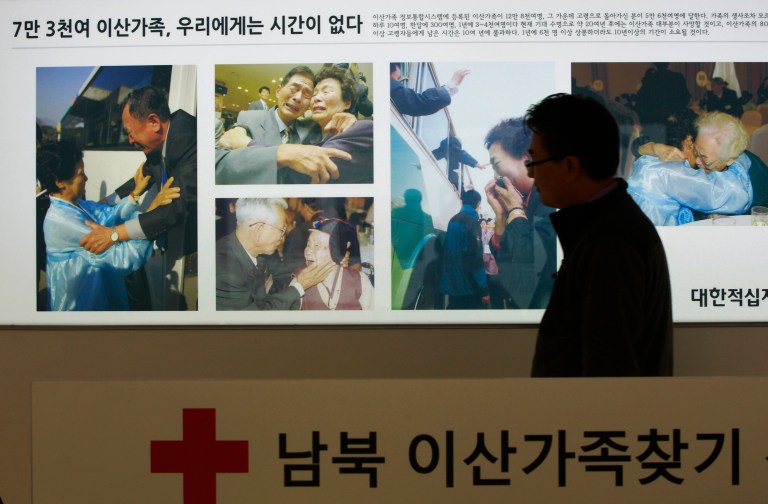 An employee of the Red Cross passes by the pictures showing some reunions of family members from North and South Korea, at the headquarters of the Korea Red Cross in Seoul, South Korea, Thursday, March 6, 2014.  Seoul said that North Korea rejected Seoul's proposal to hold talks on reunions of families divided by the 1950-53 Korean War. South Korea wants to make such reunions, which were held last month for the first time in more than three years, become regular events, but analysts say Pyongyang worries that could take away a key piece of political leverage with the South. The Korean writing at bottom reads 