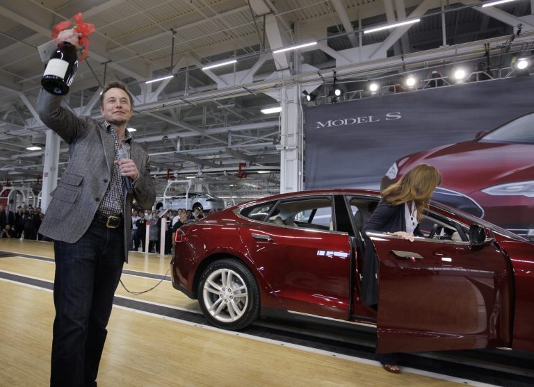 FILE - In this June 22, 2012 file photo, Tesla Motors Inc. CEO Elon Musk holds up a bottle of wine given as a gift from one of their first customers, right, during a rally at the Tesla factory in Fremont, Calif. Tesla Motors says it is preparing a site near Reno, Nevada, as a possible location for its new battery factory, but is still evaluating other locations. (AP Photo/Paul Sakuma, File)