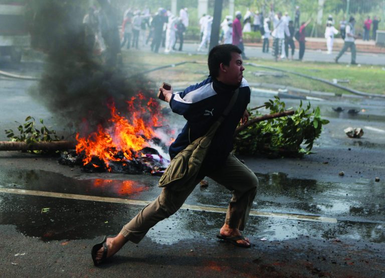 A Muslim man prepares to throw a rock at police officers during a protest against American-made film 