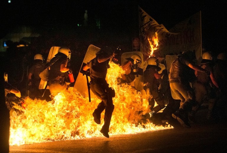 Riot police officers run through fire as anti-austerity protesters throw petrol bombs, during clashes in Athens. (AP Photo/Emilio Morenatti)