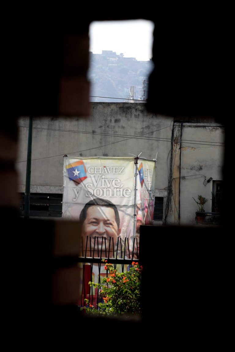 A poster of Venezuela's President Hugo Chavez is seen through a cross-shaped window, from inside the military hospital's chapel, in Caracas, Venezuela, Tuesday, March 5, 2013. A brief statement read on national television by Communications Minister Ernesto Villegas late Monday carried the sobering news about the charismatic 58-year-old leader's deteriorating health. Villegas said Chavez is suffering from 