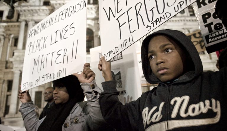 A young protester and his mother are seen holding signs at Dillworth Park at Philadelphia City Hall.