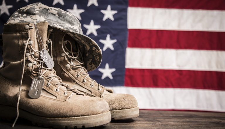 USA military boots, hat and dog tags with American flag in background.  
