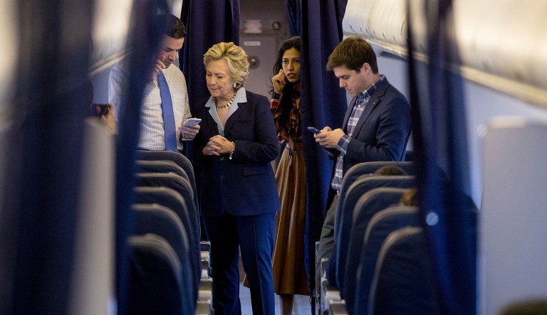 Democratic presidential candidate Hillary Clinton, accompanied by senior aid Huma Abedin, second from right, and traveling press secretary Nick Merrill, right, speaks with national press secretary Brian Fallon, left, aboard her campaign plane in White Plains, N.Y., Monday, Oct. 3, 2016, before traveling to Toledo, Ohio. (AP Photo/Andrew Harnik)