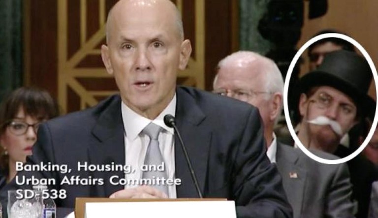 Appearing behind former CEO Richard Smith on live broadcasts of the hearing, the activist overshadowed the proceedings on social media by flaunting a tux, bowtie, and top hat while twirling a magnificent mustache. (Image courtesy screenshot)