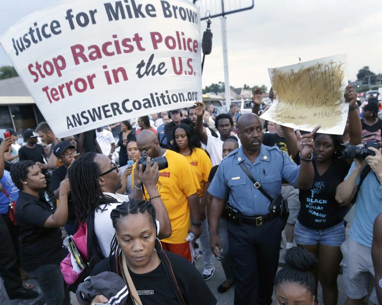In this Aug, 16, 2014 file photo Missouri Highway Patrol Capt. Ron Johnson, center right, walks among people protesting the police shooting death of Michael Brown in Ferguson, Mo. (AP Photo/Charlie Riedel, File)