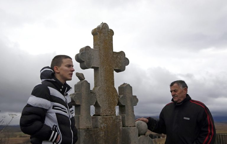 In this Feb. 5, 2014 photo, Gavrilo Princip's relatives, Nikola Princip, right, and his grandson Novak Princip,16, pay their respects at the Princip family plot in a cemetery in the village of Obljaj, near Bosansko Grahovo, 300 kilometers west of Sarajevo,  Bosnia. A century later, Gavrilo Princip still provokes controversy from beyond the grave as his legacy has been molded time and again to meet political agendas in the Balkans, still a patchwork of ethnic and religious rivalries. (AP Photo/Amel Emric)