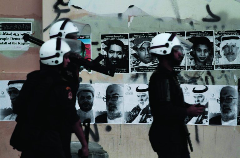 Bahraini riot policemen look for anti-government protesters during clashes in Sitra, Bahrain, Monday, Sept. 3, 2012. Pictures of people killed in the unrest and of jailed political leaders are plastered on the wall. Verdicts are expected Tuesday for numerous jailed leaders, medical workers and activists. (AP Photo/Hasan Jamali)