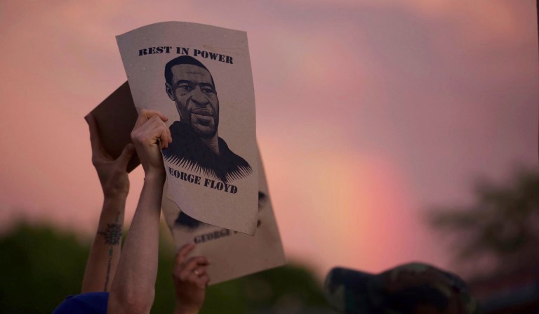 A protestor holds a sign with an image of George Floyd during a Wednesday, May 27, 2020 protest at the Minneapolis Police Department 3rd precinct. A protest was held to demand justice in the death of George Floyd, who died after a Minneapolis police officer knelt on his neck. This was the second night of protest against the killing. 