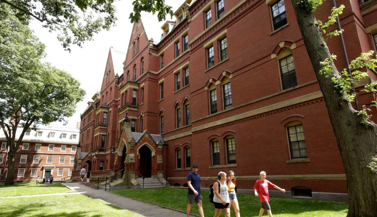 In this Tuesday, July 16, 2019 photo people walk along a sidewalk on the campus of Harvard University, in Cambridge, Mass. 