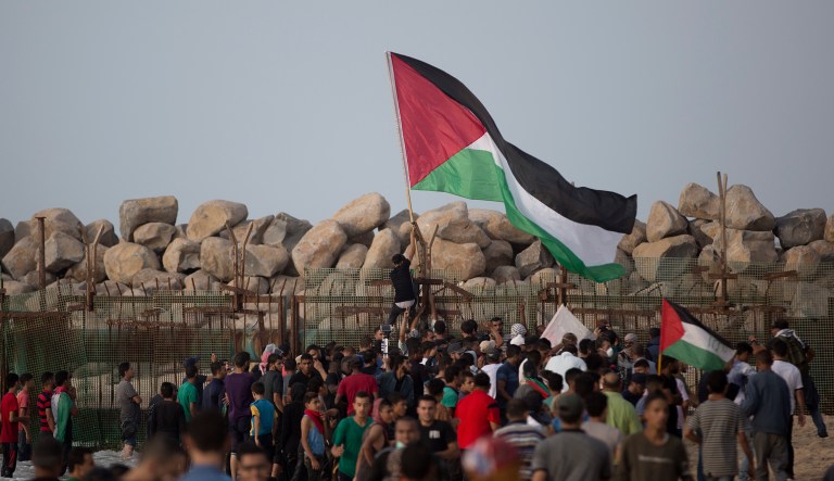 Palestinian protesters hangs a national flag at the border fence during a protest on the beach at the border with Israel near Beit Lahiya, northern Gaza Strip, Monday, Oct. 15, 2018.