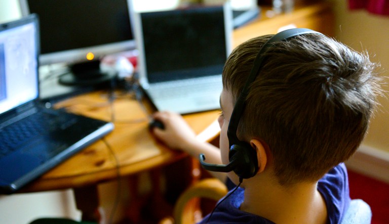 A young boy wears headphones while sitting in front of several computer monitors.