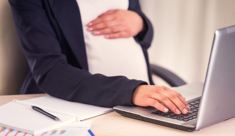 A pregnant woman uses laptop in the office.