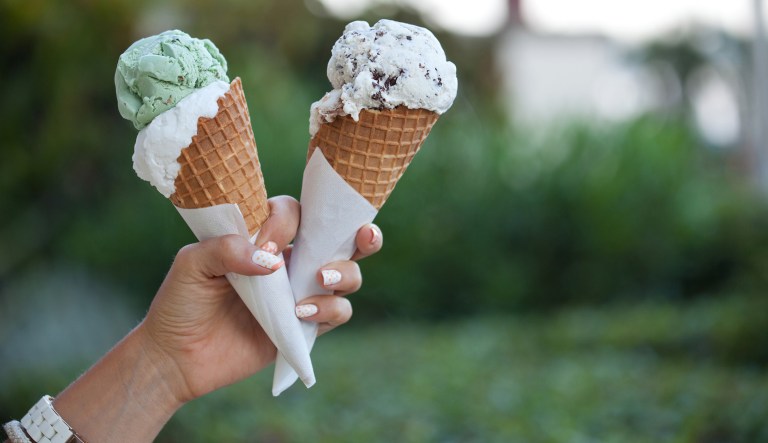 Two colorful tasty ice cream cones in hand.