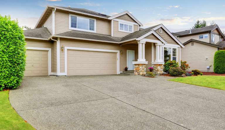 Neat, beige home with two garage spaces and large concrete driveway. 