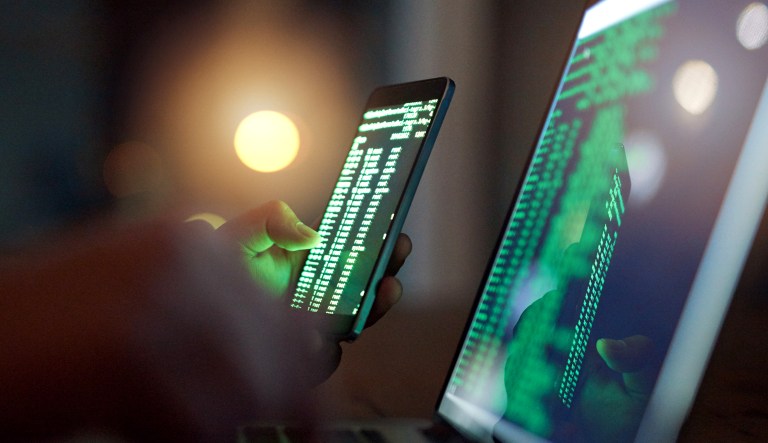 A hacker uses both a smartphone and a computer.