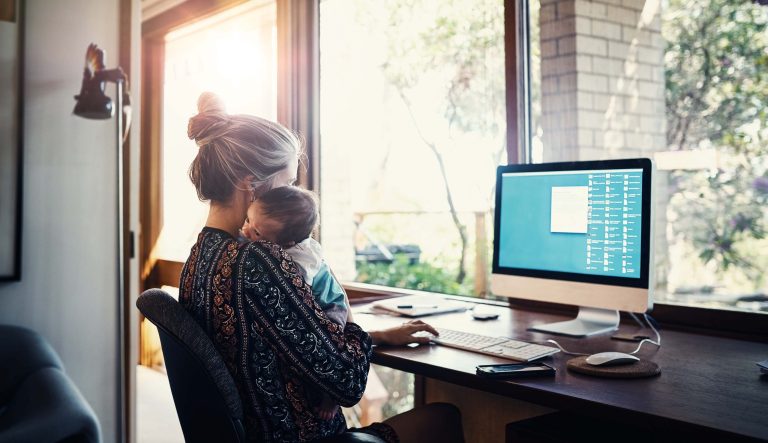 Shot of a young woman working at home while holding her newborn baby son.