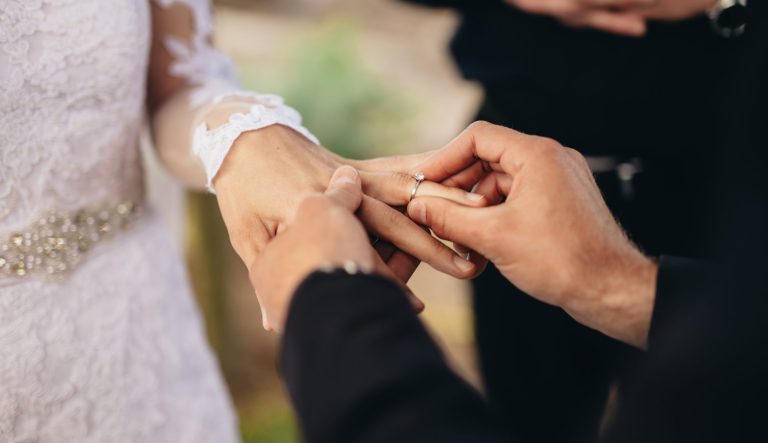 Closeup of groom placing a wedding ring on the brides hand.