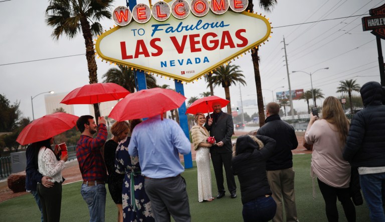 People watch as Katie Hollingshead, center, and Pat Severance get married in the rain at the "Welcome to Fabulous Las Vegas" sign on Valentine's Day, Thursday, Feb. 14, 2019, in Las Vegas.