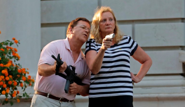 Armed homeowners Mark and Patricia McCloskey stand in front of their house along Portland Place to confront protesters marching to St. Louis Mayor Lyda Krewson's house in the Central West End of St. Louis.