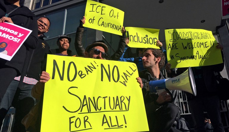 FILE - In this April 14, 2017, file photo, protesters hold up signs outside a courthouse where a federal judge was to hear arguments in the first lawsuit challenging President Donald Trump's executive order to withhold funding from communities that limit cooperation with immigration authorities in San Francisco. California state lawmakers passed and Gov. Jerry Brown signed nearly 900 new laws in 2017, most of which take effect Jan. 1, 2018. Among them is one making California a sanctuary state in response to the Trump administration's immigration crackdown.