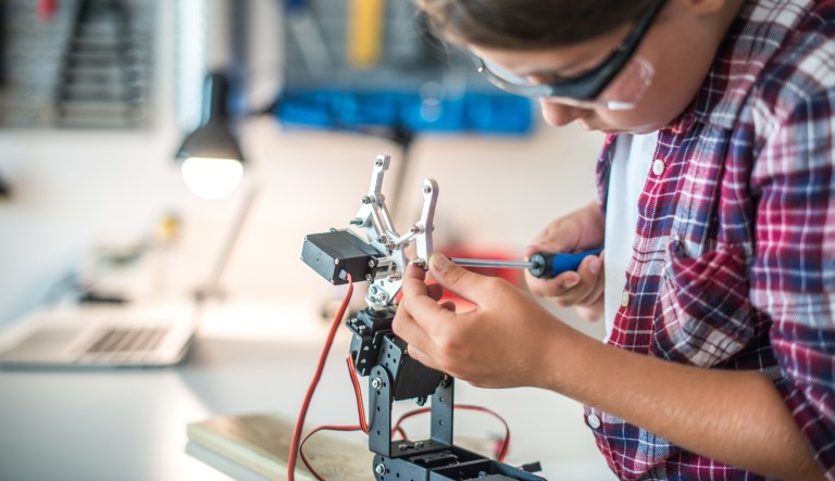 Young girl fixing a robot arm in a workshop.