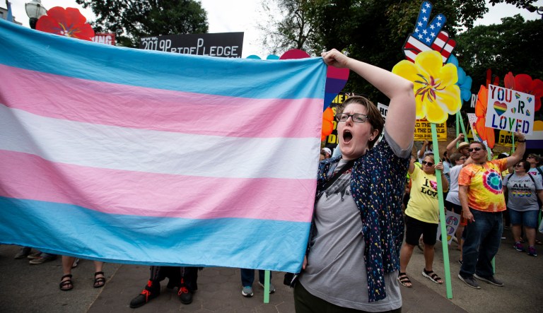 A supporter for the transgender community holds a trans flag in front of counter-protesters to protect attendees from their insults and obscenities at the city's Gay Pride Festival in Atlanta on Saturday, Oct. 12, 2019.