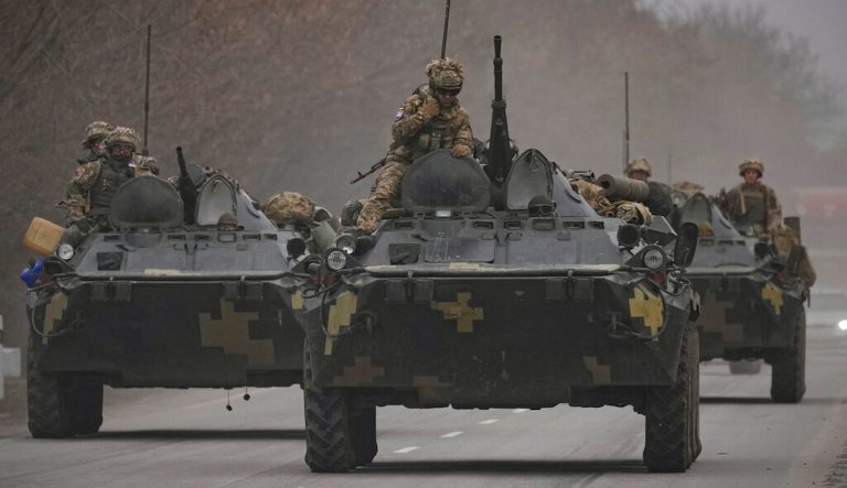 Ukrainian servicemen sit atop armored personnel carriers driving on a road in the Donetsk region, eastern Ukraine, Thursday, Feb. 24, 2022. Russian President Vladimir Putin on Thursday announced a military operation in Ukraine and warned other countries that any attempt to interfere with the Russian action would lead to 
